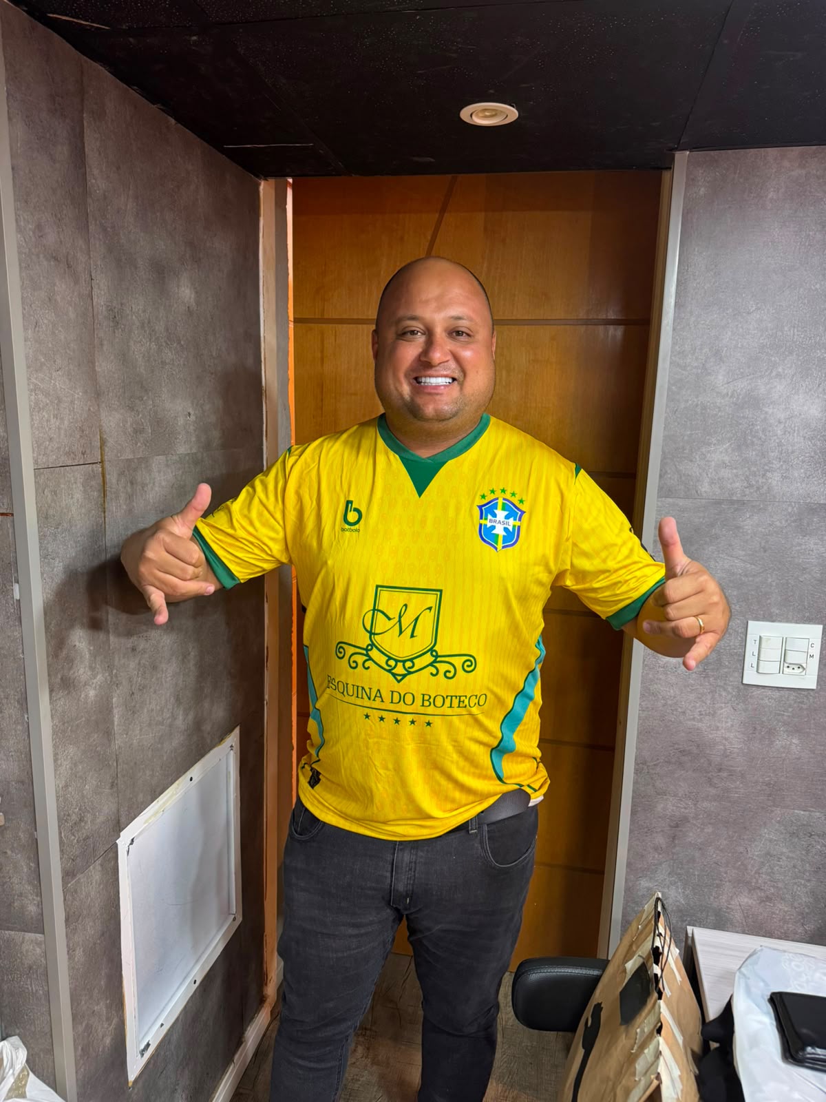 Mayco sorrindo de camisa amarela personalizada do Esquina do Boteco, com escudo M e cinco estrelas no peito